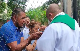 El P. Sebastián López distribuye la Eucaristía detrás de una malla, vigilado por la policía de Nicaragua. Crédito: Diócesis Media - Radio Stereo Santa Lucía 