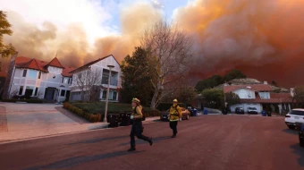 Los bomberos corren mientras un incendio forestal arde en Pacific Palisades, California, el 7 de enero de 2025. Un incendio forestal de rápido avance en un suburbio de Los Ángeles quemó edificios y provocó evacuaciones mientras vientos "potencialmente mortales" azotaban la región.