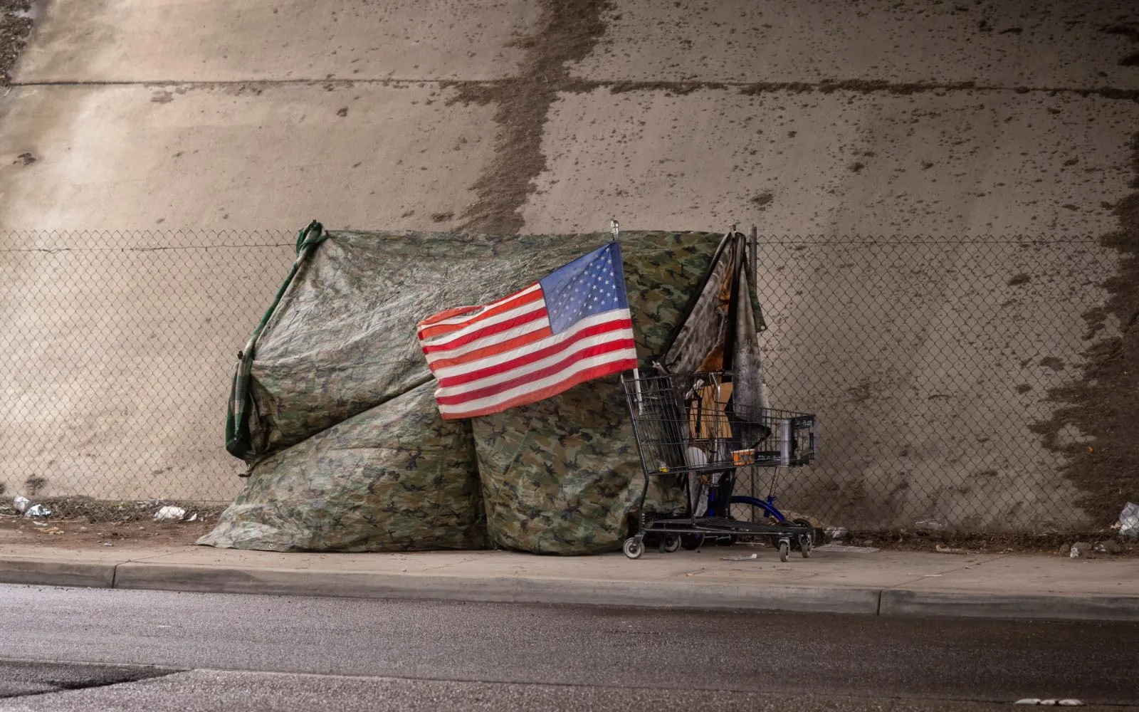 Bandera estadounidense en una tienda de campaña hecha de lona de camuflaje en un paso subterráneo de una carretera.?w=200&h=150