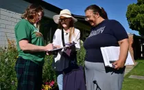 Las voluntarias Liz Grumbach (centro) y Patricia Jones se reúnen con Lucy Meyer (izquierda), quien firma una petición afuera de su casa en Phoenix el 13 de abril de 2024, mientras las voluntarias van puerta a puerta en busca de firmas para que la petición de la Ley de Acceso al Aborto de Arizona se incluya en la boleta electoral de noviembre de 2024 para que los votantes decidan.