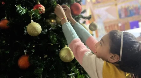 Una niña cuelga un adorno en el árbol de Navidad de la iglesia de la Sagrada Familia en Gaza.