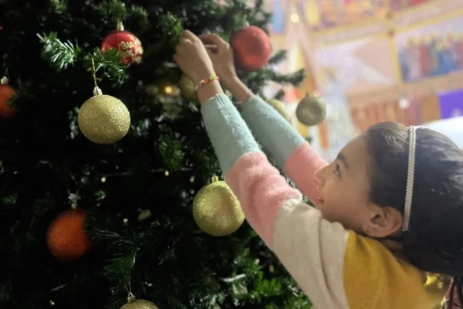 Una niña cuelga un adorno en el árbol de Navidad de la iglesia de la Sagrada Familia en Gaza.