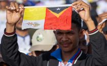 Joven de Timor Oriental levanta la bandera del Vaticano junto a la de su país en la Misa del Papa Francisco en Taci Tolu