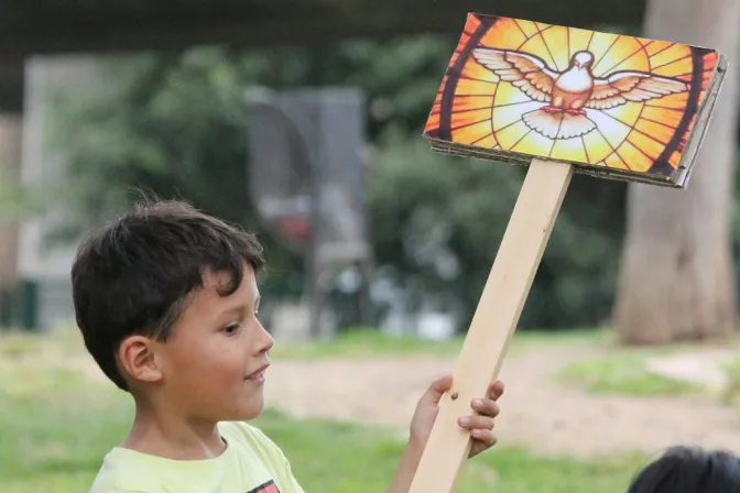 Un niño sostiene un cartel con una imagen del Espíritu Santo.