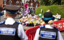 Policías de Inglaterra observan las ofrendas póstumas en memoria de las tres niñas asesinadas el lunes en  la ciudad de Southport.