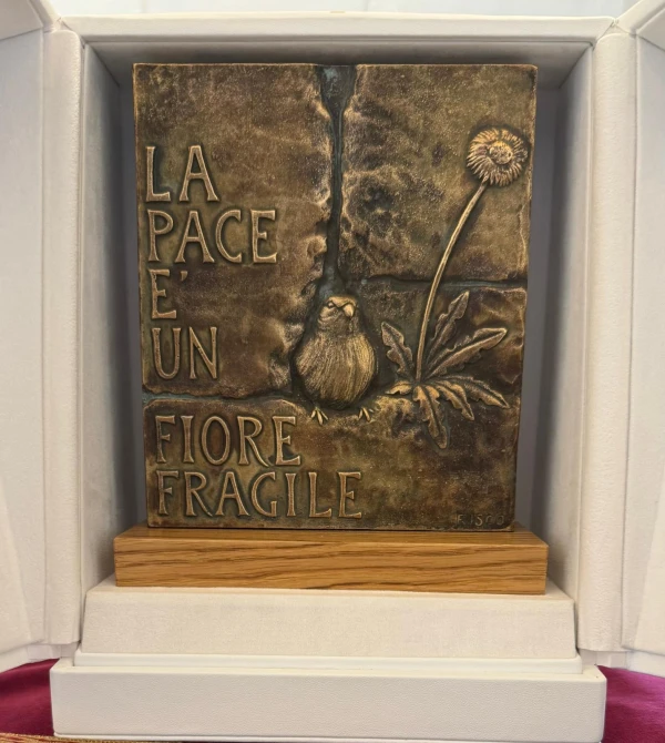 Bronce con la imagen de una flor junto a un pájaro con la inscripción “La paz es una flor frágil”. Crédito: AIGAV